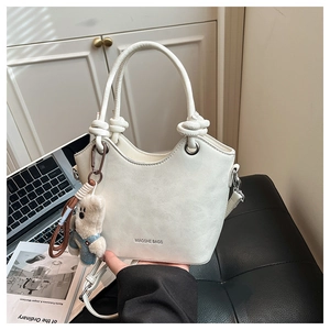 Detail of off-white bucket bag with knotted handle and plush bear charm on side