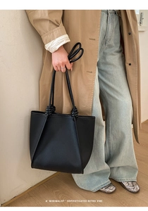 Detail of black tote bag with textured leather surface and knotted rope handle design