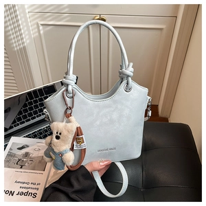 Detail of light blue bucket bag with leather texture and cute teddy bear charm accessory