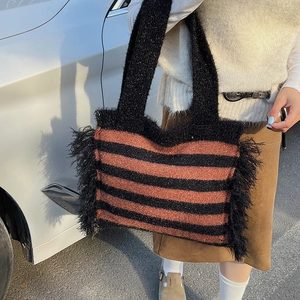 Detail of striped knitted tote bag featuring black fringe tassels and sparkling metallic yarn