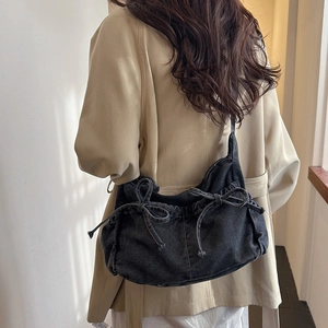 Detail of dark wash denim crescent bag featuring bow drawstrings worn with a beige trench coat