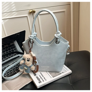 Detail of light blue bucket bag with knot handle, teddy bear charm and sleek PU texture