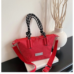 Detail of red checkered canvas handbag featuring woven rope handles and a wide shoulder strap