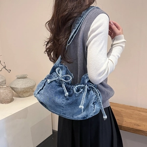 Detail of blue washed denim shoulder bag with bow drawstring on simple wabi-sabi background