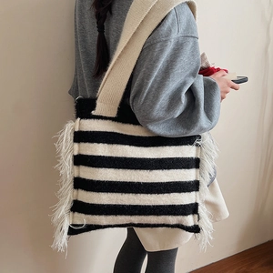 Fashionable black and white striped knitted tote bag with white side tassels worn by a model