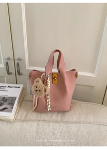 Detail of pink leather bucket bag with gold turn-lock, bear charm, and woven rope decoration