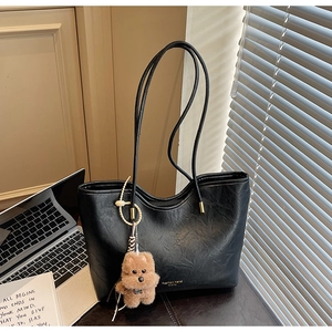 Close-up of black pebble texture tote bag with gold logo and plush puppy charm