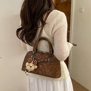 Detail view of vintage brown matte handbag featuring a cute plush bear pendant accessory