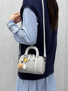 Light gray Boston bag with plush charms shown as a crossbody on a stylish model