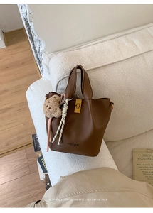 Detail of brown leather bucket bag with gold clasp, teddy bear charm and woven knot strap