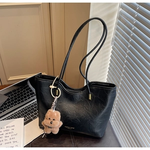 Detail of black faux leather tote bag with gold hardware and brown bear charm on a desk