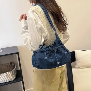 Detail view of denim shoulder bag with bow drawstring on model in home setting