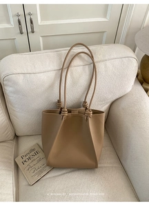 Detail of khaki lychee grain leather tote bag with knotted strap on a soft fabric sofa