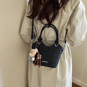 Detail view of black pebble leather bucket bag with cute bear charm and woven strap accessory