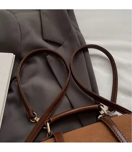 Detail of retro brown leather backpack showing long shoulder straps and gold metal hardware