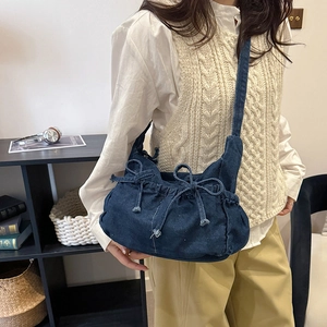Detail of dark blue denim shoulder bag with decorative bow drawstring in lifestyle setting