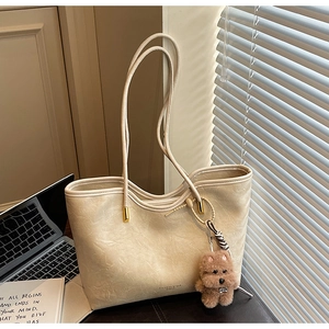 Detail of beige tote bag with soft leather texture, gold hardware and teddy bear charm
