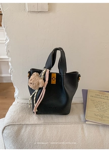 Detail of black lychee grain leather bucket bag with gold clasp and bear charm decoration