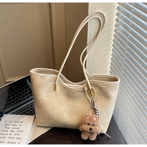 Close-up of beige leather tote bag featuring thin straps and cute brown plush puppy charm