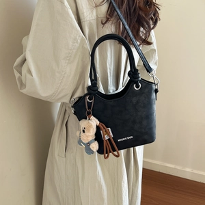 Detail view of black pebble leather bucket bag with teddy bear charm and logo