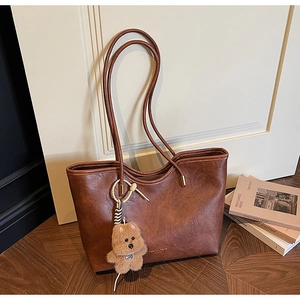 Close-up of brown pebbled leather tote bag with gold lettering and cute bear charm