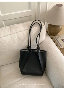 Detail view of black lychee-textured leather tote bag with knotted shoulder strap decor
