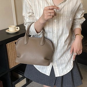 Close-up of taupe litchi texture leather handbag featuring dual handles and fine stitching