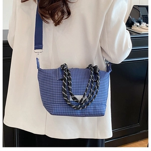 Detail of blue plaid canvas handbag with woven rope handle and fashion label on model