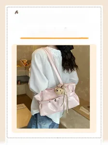 Pink glossy leather tote bag with teddy bear charm shown on model in a cozy cafe setting