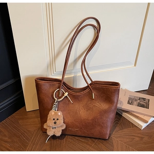 Detail of caramel faux leather tote bag with plush bear charm on wooden floor