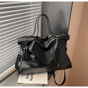 Detail of black tote bag with silver rivets, tassel charm and front zipper pocket