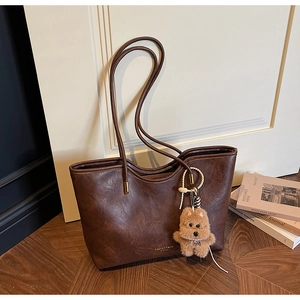 Close-up of deep brown leather tote bag with gold branding and cute plush dog charm