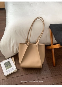 Macro detail of beige tote bag showing lychee grain leather and artisan knot shoulder straps