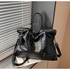 Detail of black glossy leather tote bag featuring silver rivets and tassel charm