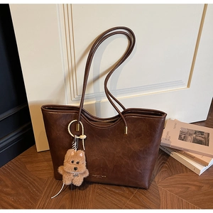 Detail of vintage brown leather tote bag with plush puppy charm against white door