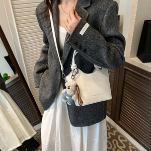Detail view of a white glossy leather bucket bag featuring a cute plush bear pendant accessory