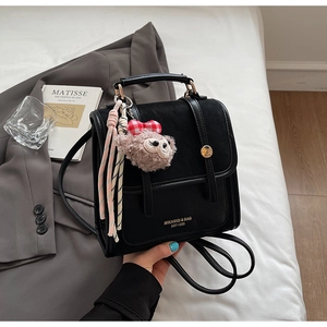 Close-up of black PU backpack featuring vintage buckle straps and a plush charm detail