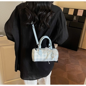 Détail d'un sac cylindre à carreaux bleus avec nœud en dentelle et perle en bandoulière