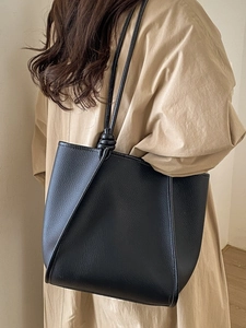 Minimalist black lychee leather tote bag with unique knotted strap design for daily commute