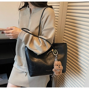 Detail of black leather tote bag with brown plush puppy pendant and golden brand logo