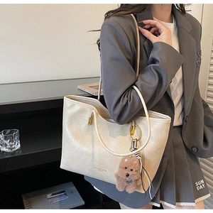 Detail of off-white faux leather tote bag featuring golden hardware and a bear charm accessory