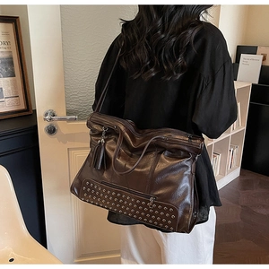 Detail view of large brown tote bag showing rivet base decoration and leather tassels