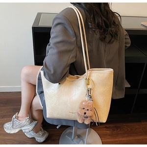 Detailed view of beige tote bag with pleated texture and cute brown plush bear charm