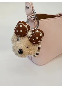 Detail of plush puppy bag charm with polka dot bow and colorful beads on a leather bag