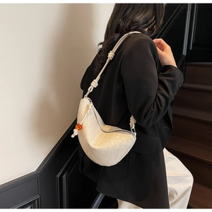 Detail of cream woven dumpling bag with unique knot shoulder strap and orange bead accent