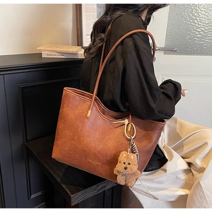Detail of caramel vintage tote bag with plush puppy pendant and long shoulder straps