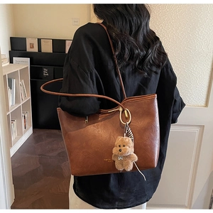 Detailed view of caramel brown tote bag with plush bear charm worn by a model