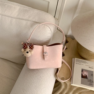 Detail of light pink leather bucket bag with cute plush bear charm on a cream sofa