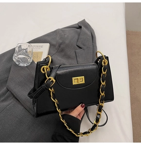 Détails d'un sac à bandoulière noir brillant avec chaîne dorée posé sur un blazer gris chic