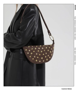 Detail of a dark brown half-moon shoulder bag with golden rivets worn by a model in a leather suit